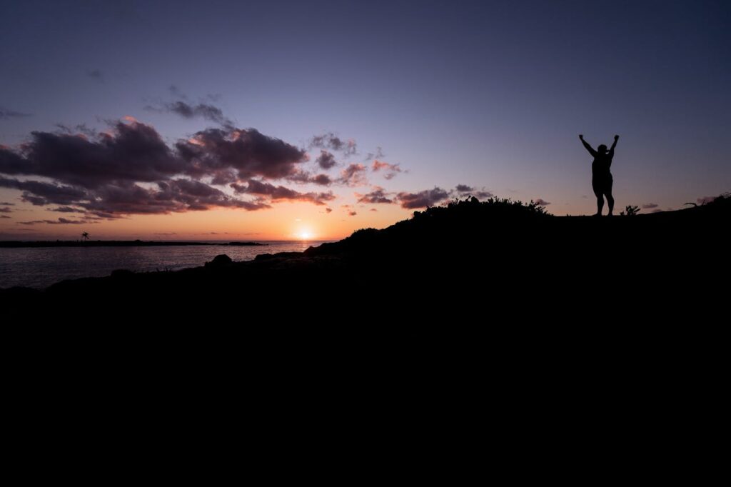 Silhouette of a person celebrating at a stunning sunset by the ocean.