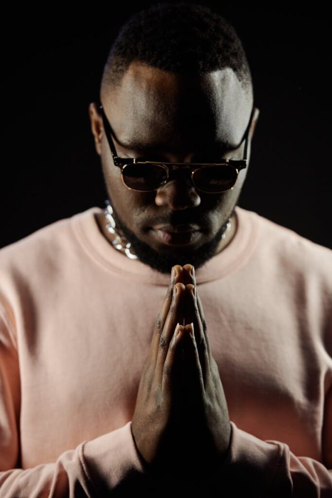 Close-up portrait of a man with sunglasses in a prayer pose. Dramatic lighting and focus on the face.